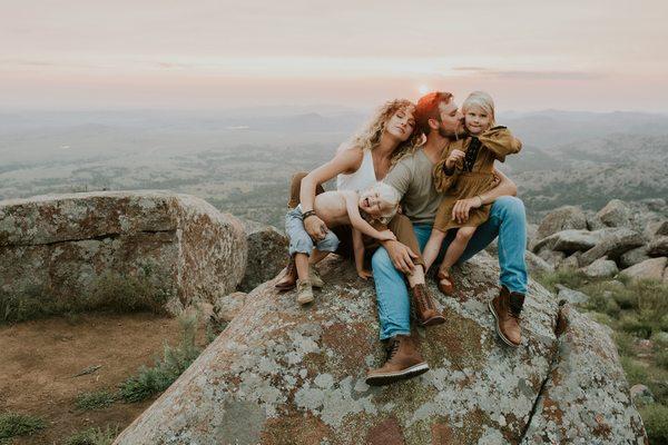 gorgeous family of four sitting on top of a rock in front of a beautiful sunset with Paige Rance Photography