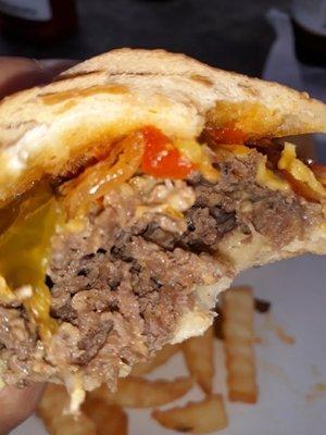 A partially devoured cheesesteak with fried onions and hot peppers