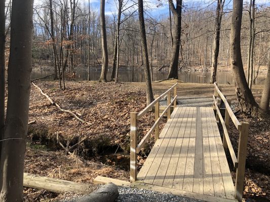 Wooden bridge to Yellow-blazed trail around earthen reservoir.