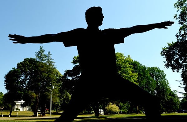 Action shot of Alistair in a Warrior II pose whilst teaching his Yoga class on the Madison Town Green.