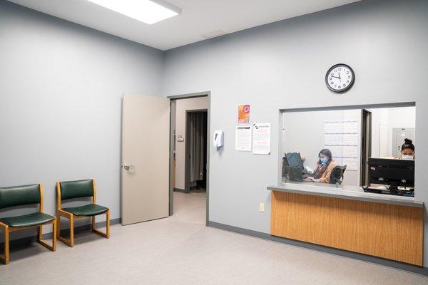 Waiting room with chairs. A woman sits at a computer behind a reception window