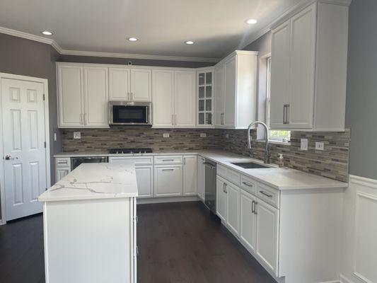 Stylish & functional kitchen featuring quartz countertops, a full line of kitchen cabinets, engineered wood flooring & mosaic backsplash!