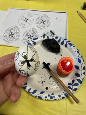 The egg drawing in the initial steps, the beeswax (dyed black), tool for drawing and candle for melting beeswax.