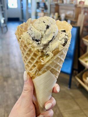 One scoop of cake batter and one scoop of cookies and cream on a vanilla waffle cone