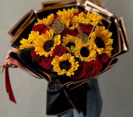 A floral arrangement of perfect roses and sunflowers, elegantly wrapped in black paper.