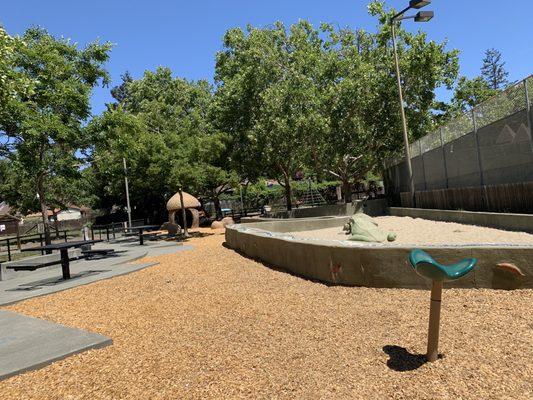 Area for 2-5 has a sand area, acorn house, giant xylophone, and one disc swing. The wall around the sand area has a water feature