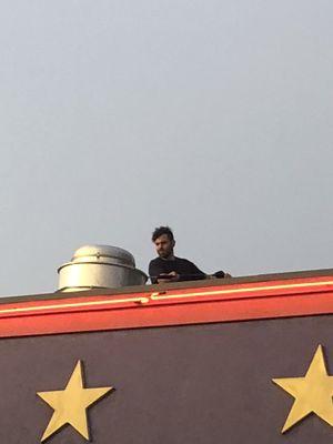 Crew member cleaning fan on the roof of a restaurant.