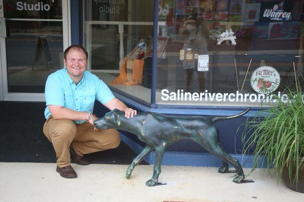 Owner Rob Reep kneeling next to the pointer statue, Rex, near the Rob Reep Studio storefront on Main Street.