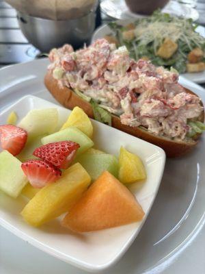 Lobster roll with fruit and a side Caesar salad