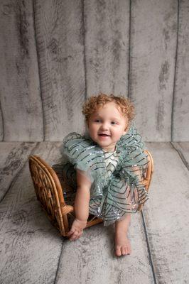 Baby girl wearing a sparkly sage outfit sitting in a bamboo prop during her cake smash session