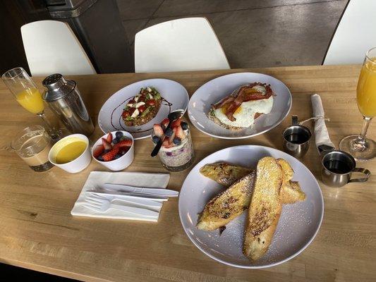 Brunch items: French toast, avocado toast with egg and bacon, caprese avocado toast, overnight oats with berries, latte drink, and mimosas.