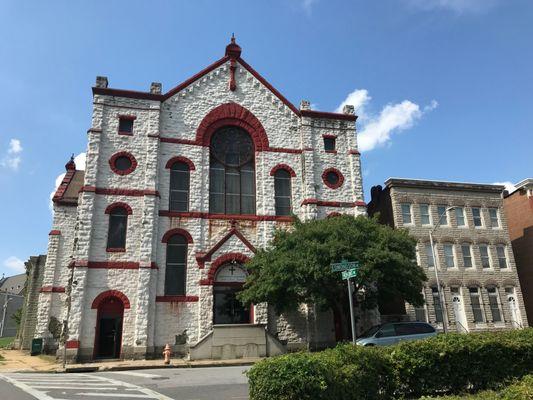 The front of a stone church building on Edmondson Avenue next to a small group of form-stone covered three-story rowhouses.