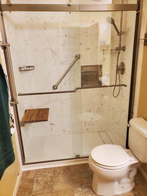 Aging in place shower with solid surface carrara marble surround, fold down seat, grab bars, niche, shower wand and bypass door