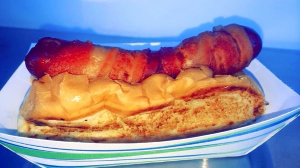 Hot dog wrapped in bacon, deep fried and topped with warm onions and melted cheese