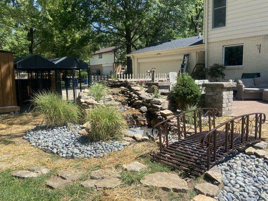 Serene backyard oasis featuring a charming iron bridge over a rock-lined pond