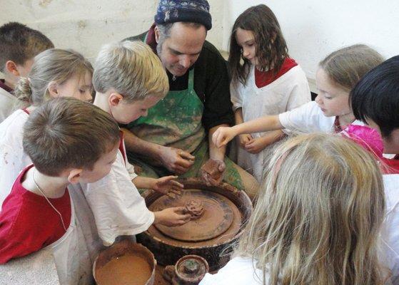 Resident potter Charley Pritchard demonstrates wheel turning to a group of school children.