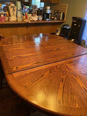 Large oak table with footed pedestal and 6 wooden chairs moved and placed where I needed it.