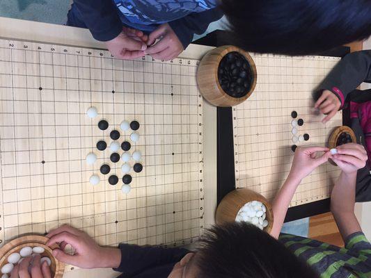 Kids playing "Connect 5" on a weiqi (Go) board in game room area.