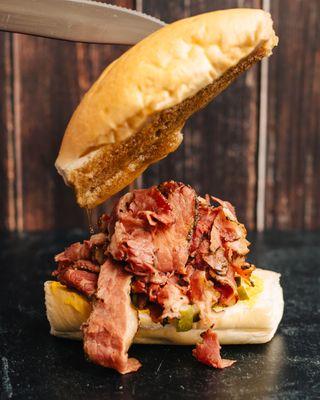 Pastrami Dip on a roll with yellow mustard and pickles then dipped in pastrami au jus