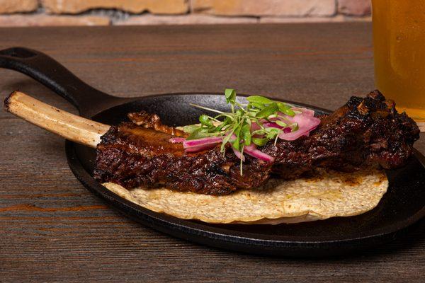 Bad to the Bone - Braised Bone-in Beef Rib in adobo falling off the bone. On a handmade corn tortilla with au jus, topped w/ pickled onions