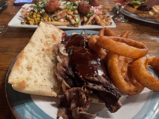 Tri tip sandwich with onion rings and cowboy fries in the back