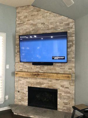 65" TV with Sonos sound bar installed on a stone faced mantle.