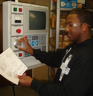 Implementing classroom knowledge to the machine.  This student is reading a blueprint while running the machine.