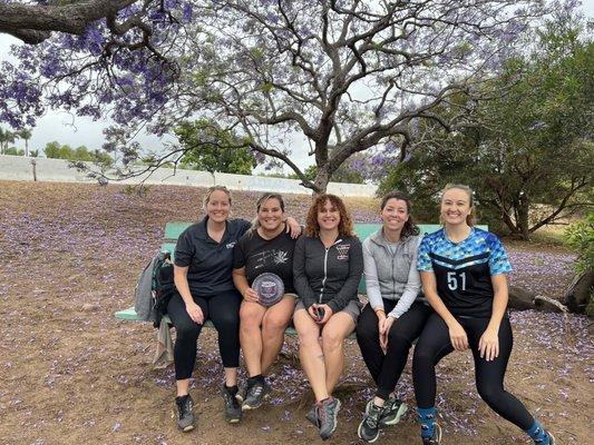 Disc golf girls in the midst of playing a tournament stopping for a quick photo while under the vibrant Jacaranda trees of Morley Field.