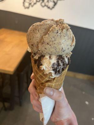 2 half-scoops of City That Never Sleeps (top) and Sundae Fundae (bottom) on a waffle cone.