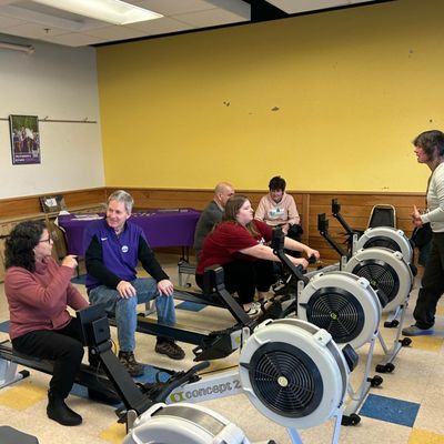 People sit with coaches on rowing machines in the indoor meeting space and multipurpose room at Holyoke Rows