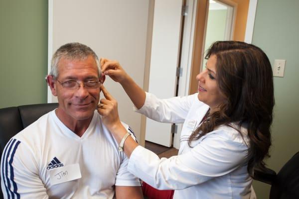 Dr. Kamal Elliot, Au.D. placing hearing devices on a patient.