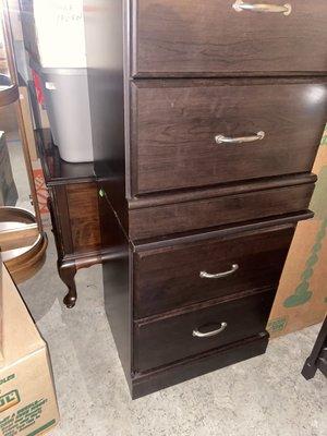 Stacked cabinet on another cabinet. In the back, tubs and boxes are stacked on a cherry end table