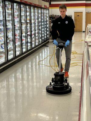 A cleaning tech uses a burnisher to shine the floors of a grocery store.