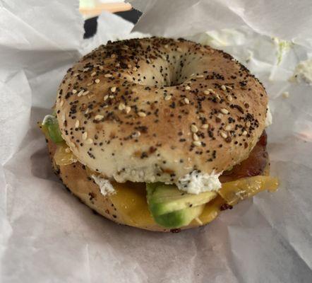 A Delicious Toasted Bagel Sandwich with bacon, cheese,avocado, cream cheese and pesto