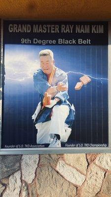 Photo on window of Grandmaster Kim breaking bricks with one hand while holding the bricks with the other hand (speed break).