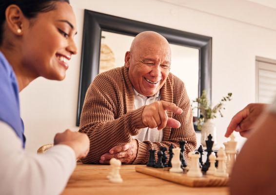 In-home caregiver companion providing social isolation care by playing chess with Senior man.