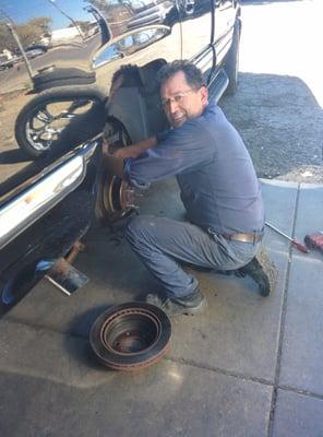 One of the workers working hard on a brake pad and drum replacement.