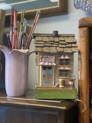 A gorgeous cute house that is handmade quilt shop with an antique flower vase holding knitting needles