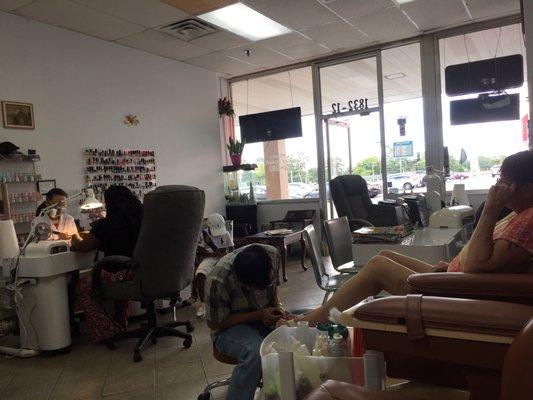 From the inside, two employees; one doing a manicure, and the other doing a pedicure.