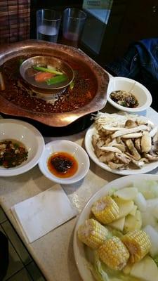 Two flavors of hot pot - Sichuan-style (outer ring) and classic (inner pot), with assorted mushrooms and assorted vegetable plates.