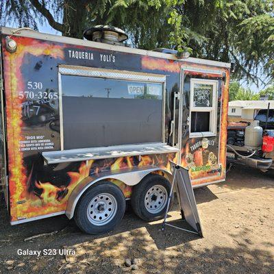 Trailer  parked in the shade on the side of the lot.