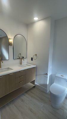 Double vanity installation, sconce, recessed lighting, black matte receptacle, and ADA approved toilet installation