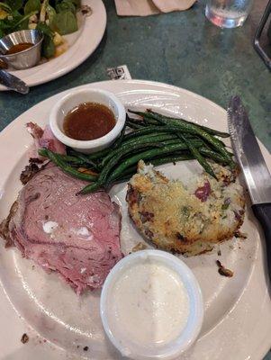 Partial eaten med rare prime rib, red potato cake and green beans.