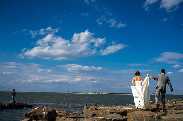 Bride and groom walk along rocks next to ocean in Long Beach Island, NJ.