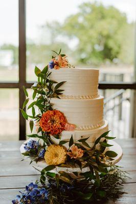 Three-tier plain white wedding cake with some greenery and colorful flower decorations