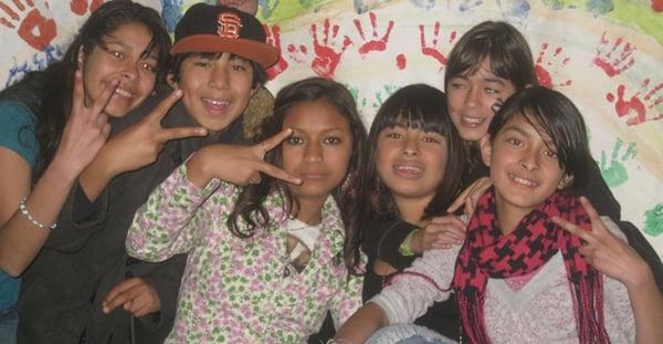 Youth holding peace signs while sitting in front of a painting they made.