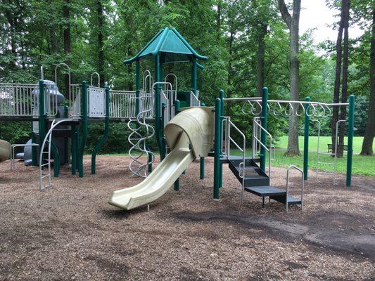 The other playground seeming for older children. Lots of trees around. Swings, pavilion and trash cans nearby.