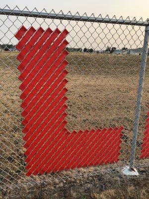 Fence art of the snap-in-place ribbon type spelled out "Learn Today Lead Tomorrow".