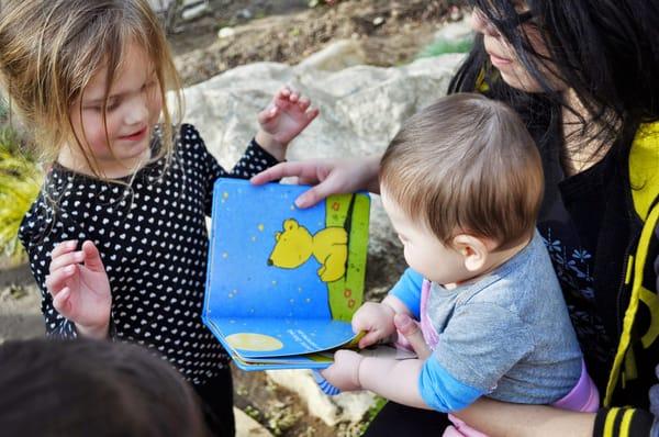 An infant and preschooler reading together with CPCC staff at a Scholastic books event