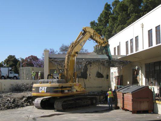 Excavator with breaker demolishing loading dock roof structure